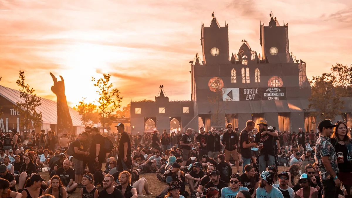 Vue aérienne d'une foule dense devant la scène principale d'un festival metal en plein air, lumières de concert et scène monumentale
