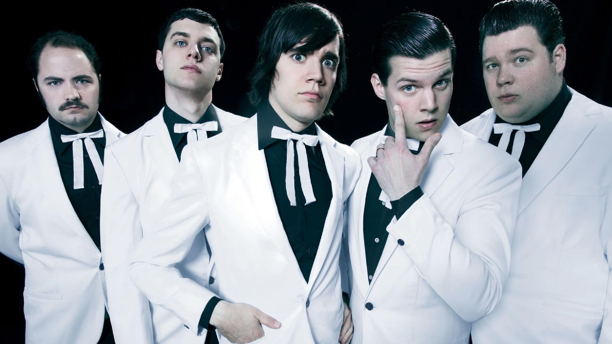 The Hives : histoire, membres et albums du garage rock suédois The Hives en concert, membres du groupe alignés sur scène sous des lumières blanches