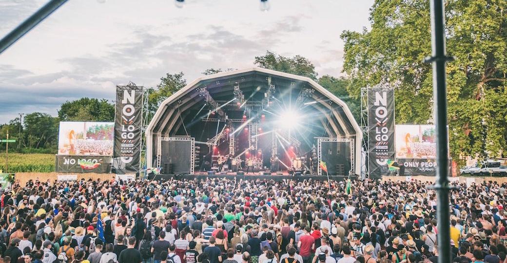 Scène du Sylak Open Air en début de soirée, public dispersé sur la pelouse, projecteurs violets et bleus, équipements son en avant-plan