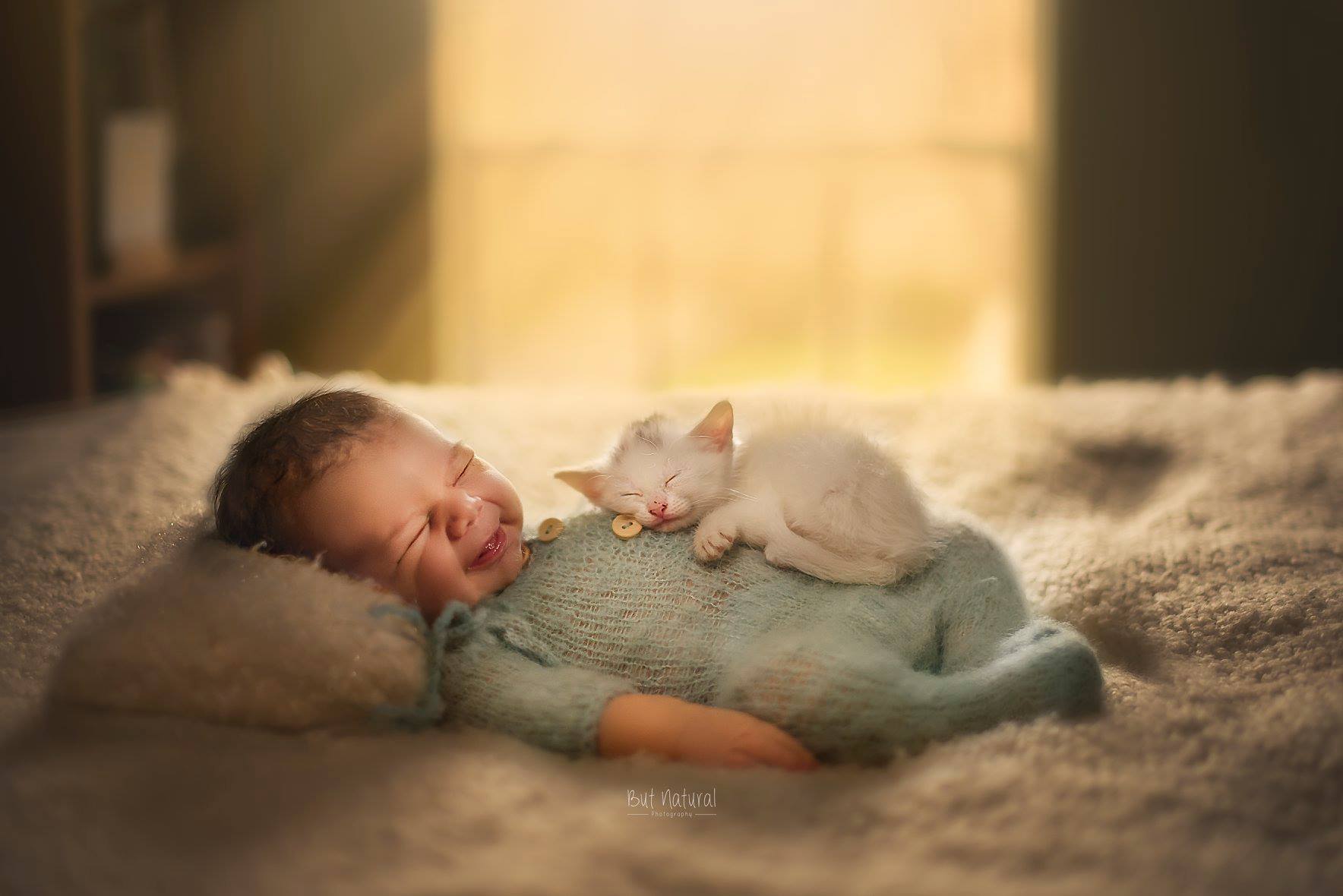 a baby sleeping with a kitten on its back
