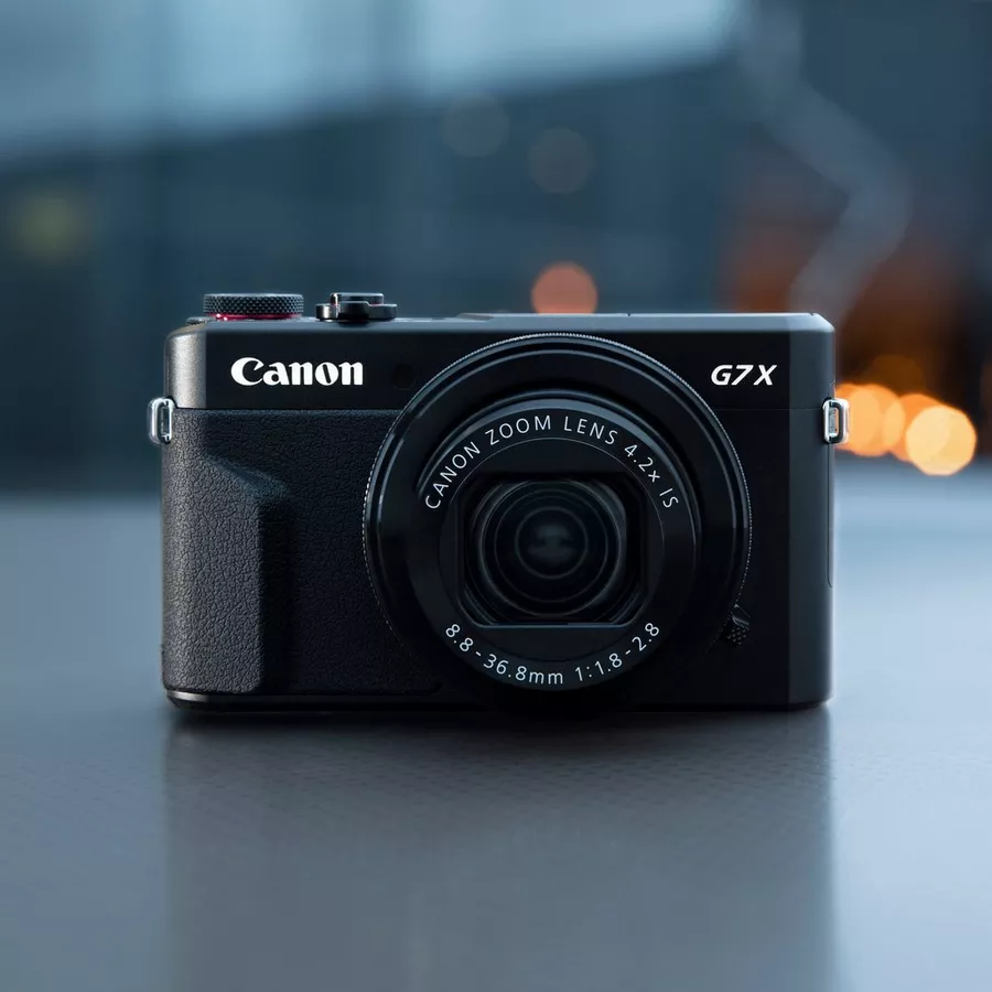Canon G7X : avis d'un pro pour le concert et le voyage Boîtier Canon G7X vu de face, posé sur une surface sombre, objectif sorti, lumière studio douce