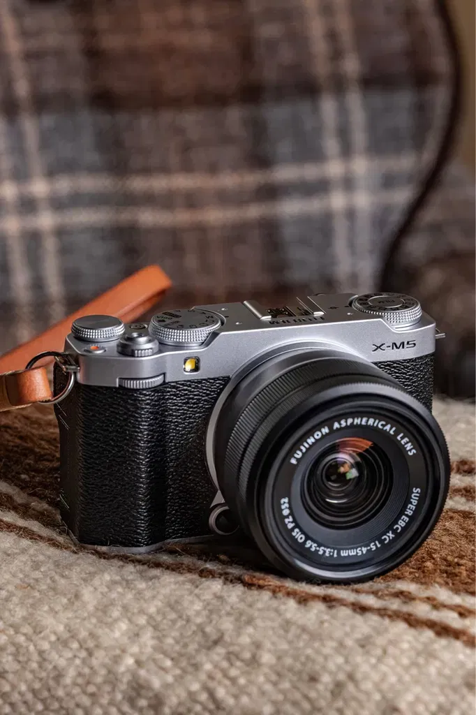 Portrait serré du Fujifilm X-M5 sur fond blanc, objectif Fujinon monté, détail des commandes