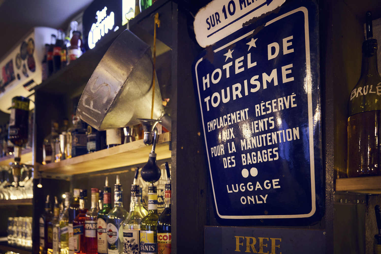Étagère du bar avec bouteilles et plaque émaillée vintage, décor de La Distillerie